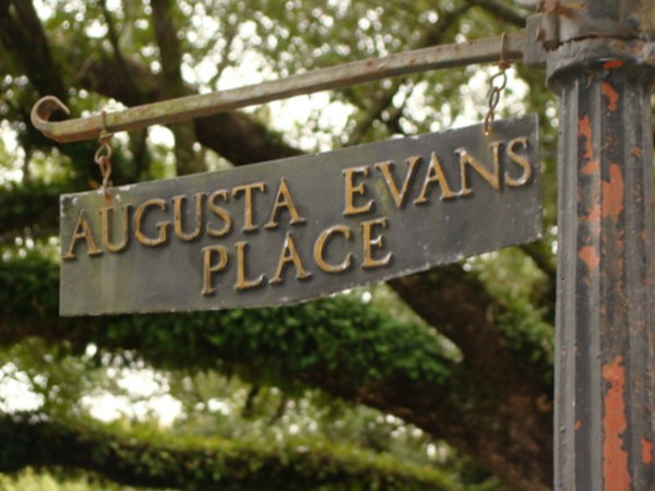 The aging sign hides Augusta Evans Place among huge oak trees.