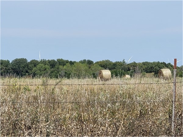 Wind turbines in the far distance and hay bales in a field 